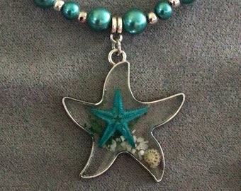 May include: A silver necklace with a teal starfish pendant and matching earrings. The pendant and earrings feature a teal starfish with a clear resin background and small seashells.