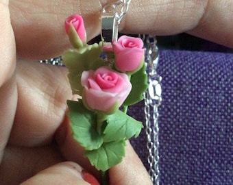 May include: A silver chain necklace with a delicate charm featuring three pink roses with green leaves.