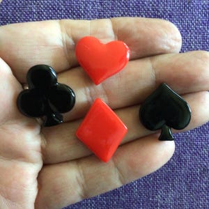 Op de afbeelding: Vier speelkaartsieraden: een rood hart, een rode ruit, een zwarte klaver en een zwarte schoppen. De bedels zijn klein en glanzend, perfect voor knutselen of het maken van sieraden.