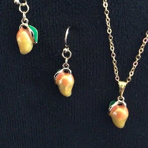 Peut inclure: Un collier en chaîne dorée et une paire de boucles d'oreilles avec des pendentifs en forme de mangue. Les pendentifs en forme de mangue sont jaunes et orange avec des feuilles vertes.