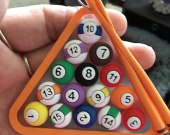 May include: A miniature orange felt triangle rack with 15 colourful billiard balls numbered 1 through 15. The rack is accompanied by two orange pool cues.