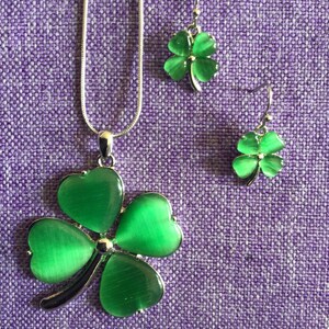 May include: A silver necklace and earrings set featuring green four-leaf clover charms. The clovers have a shiny, iridescent finish.