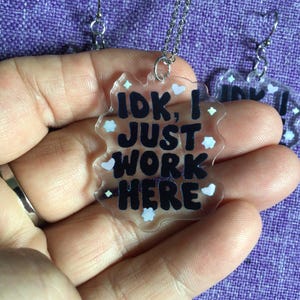May include: A clear plastic necklace and earrings set with a silver chain and black text that reads "IDK, I just work here". The pendant and earrings are decorated with small white and light blue hearts.