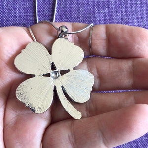 May include: A silver four-leaf clover pendant necklace. The pendant is detailed with a textured finish and a small, clear stone in the center.
