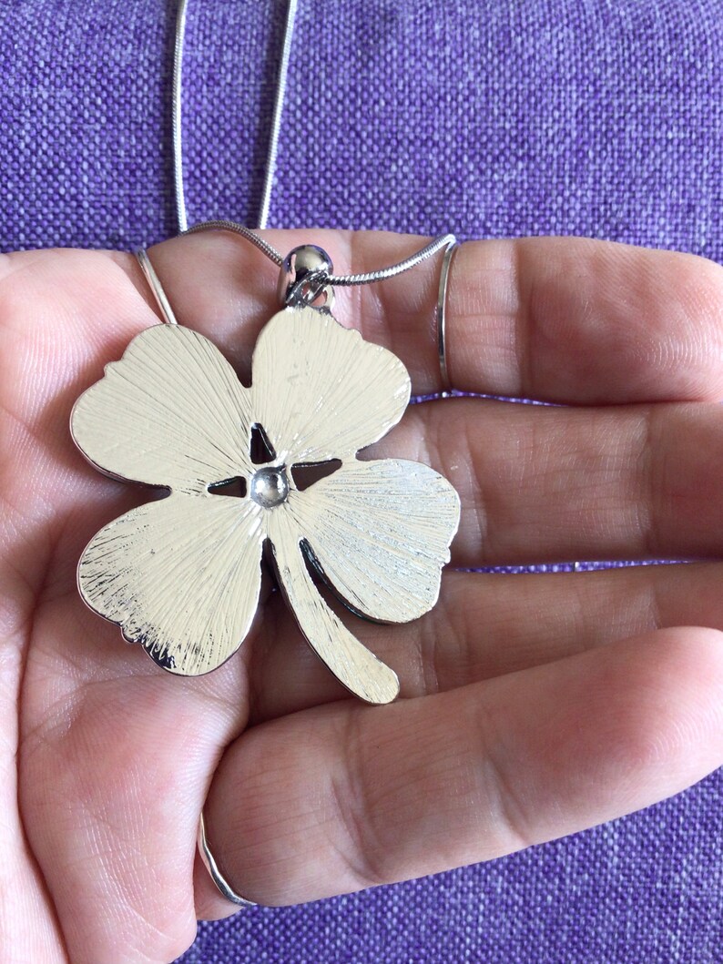 May include: A silver four-leaf clover pendant necklace. The pendant is detailed with a textured finish and a small, clear stone in the center.