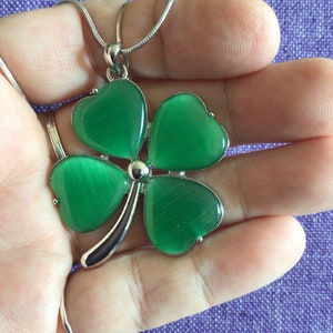 May include: A silver chain necklace with a green four-leaf clover pendant. The clover is made of faceted glass and has a shiny, iridescent finish.