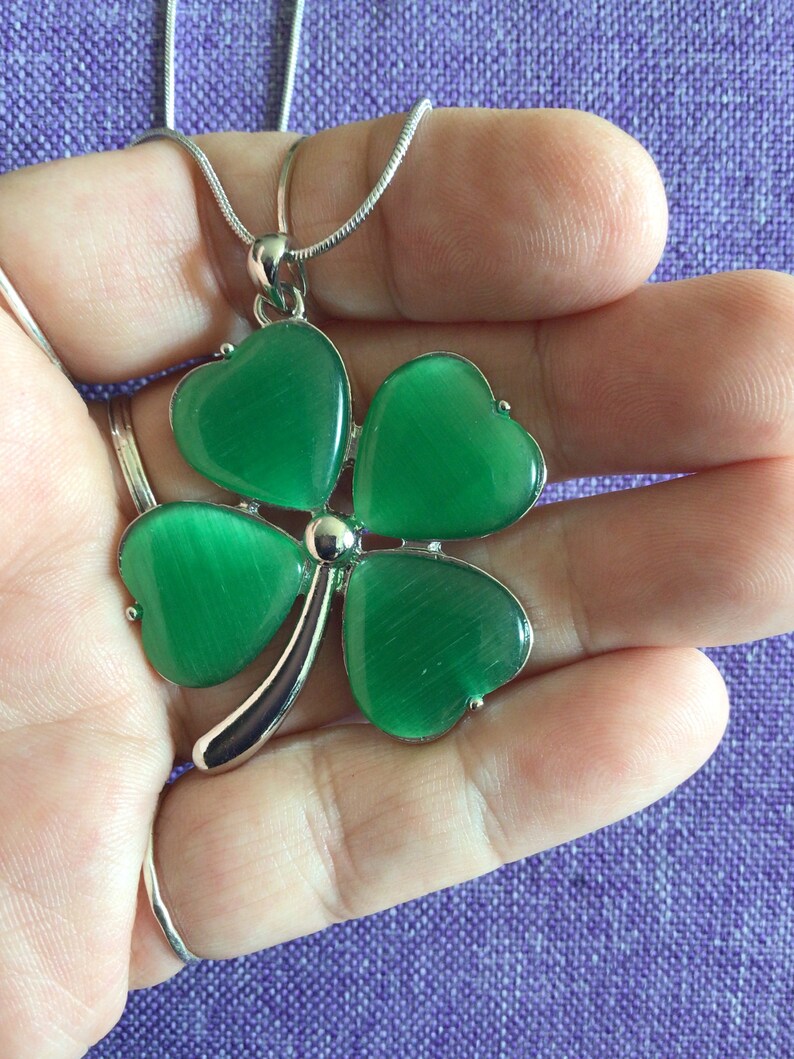 May include: A silver chain necklace with a green four-leaf clover pendant. The clover is made of faceted glass and has a shiny, iridescent finish.