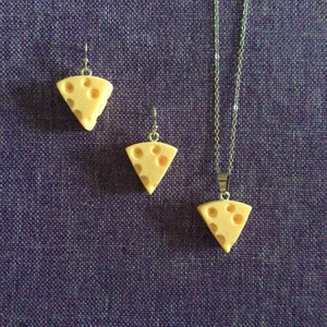 Peut inclure: Un ensemble de trois pendentifs en forme de fromage, comprenant un collier et des boucles d'oreilles. Les pendentifs sont en matériau jaune clair et ont une texture de fromage réaliste avec des trous. Le collier a une chaîne argentée.