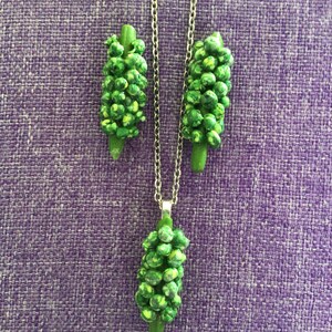 Puede incluir: Un conjunto de collar y pendientes verdes con un racimo de pequeñas cuentas verdes. El collar tiene una cadena de plata y los pendientes están unidos a postes de plata.