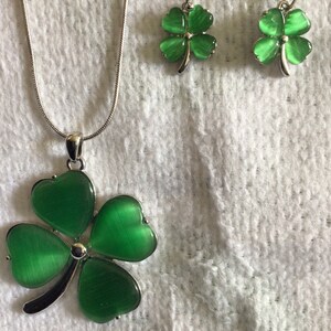 May include: A silver necklace and earrings set with green four-leaf clover charms. The charms have a shiny, iridescent finish.