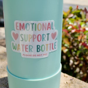 May include: A light blue water bottle with a sticker that says "Emotional Support Water Bottle" with two pink hearts and the text "Please Do Not Pet".