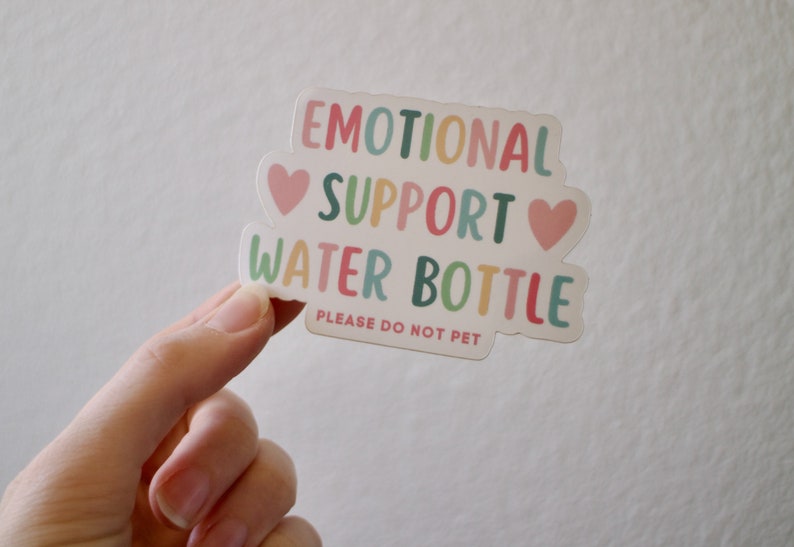 May include: A white sticker with the text "Emotional Support Water Bottle" in colourful letters. Two pink hearts are on either side of the word "Support". The text "Please do not pet" is printed in smaller letters below the main text.
