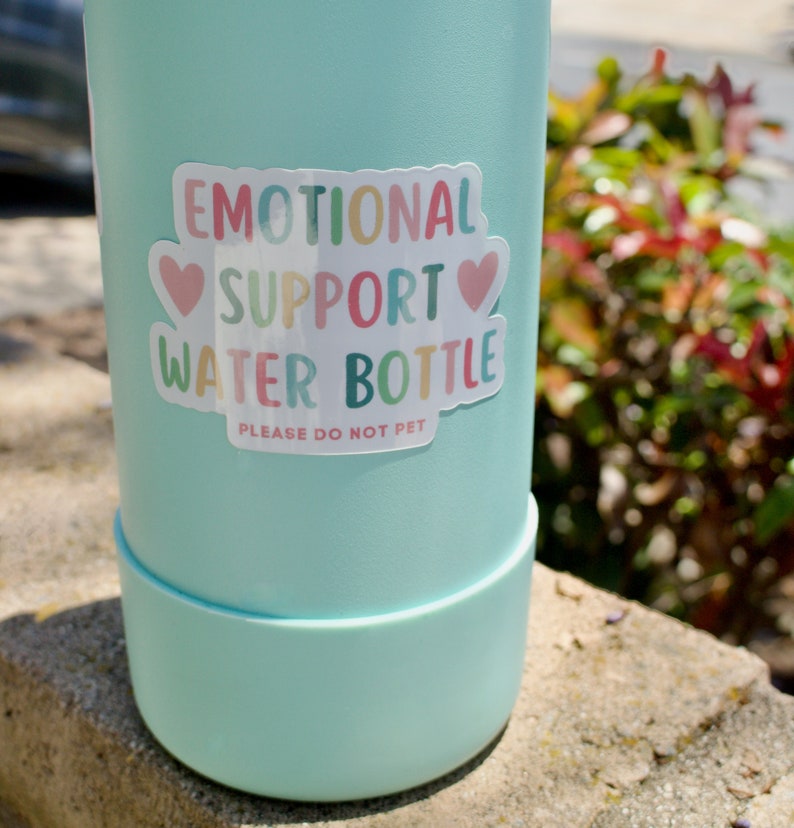 May include: A light blue water bottle with a sticker that says "Emotional Support Water Bottle" with two pink hearts and the text "Please Do Not Pet".