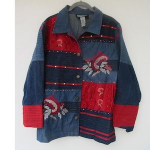 May include: A denim jacket with a patchwork design featuring red and blue panels. The jacket has floral embroidery, gold-colored button closures, and red ribbed cuffs. The collar is denim, and the jacket is hanging on a gray hanger.