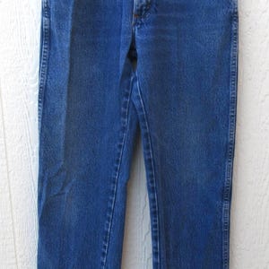 May include: Classic blue denim jeans with a straight leg cut. The jeans feature traditional five-pocket styling, a button and zipper closure, and belt loops. The garment is hanging on a metal hanger.