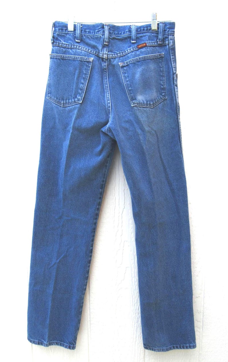 May include: Blue denim jeans with a classic five-pocket design. The jeans have a straight leg cut and are hanging from a hanger. The back pockets and waistband are visible. The jeans are made of a durable denim material.