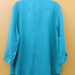 May include: A turquoise button-down shirt with long sleeves, cuffed at the elbows. The shirt has a collar and a yoke detail on the back. The fabric appears to be a lightweight material, suitable for warmer weather.