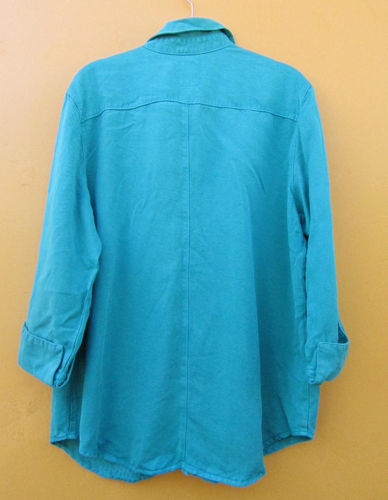 May include: A turquoise button-down shirt with long sleeves, cuffed at the elbows. The shirt has a collar and a yoke detail on the back. The fabric appears to be a lightweight material, suitable for warmer weather.