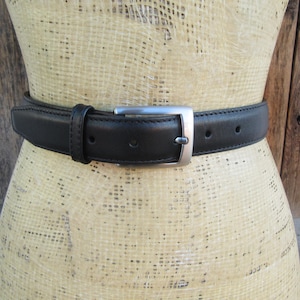 Pode incluir: Um cinto de couro preto com uma fivela retangular prateada. O cinto &eacute; usado em volta de um manequim. O cinto tem v&aacute;rios orif&iacute;cios para ajuste. O cinto tem cerca de 3,8 cm de largura.