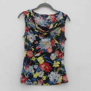 Op de afbeelding: Een mouwloze top met een boothals en een levendig bloemenpatroon op een donkerblauwe achtergrond. De print bevat diverse bloemen in tinten rood, geel, lichtblauw en wit. Het label aan de binnenzijde vermeldt Chaps Sport maat S.