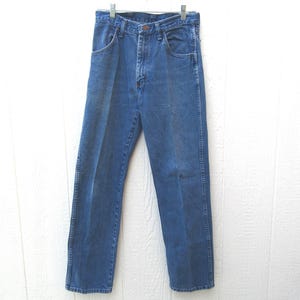 May include: Blue denim jeans hanging on a metal hanger. The jeans have a classic five-pocket design, a button and zipper closure, and a straight leg fit. The denim is a medium wash, showing some fading.