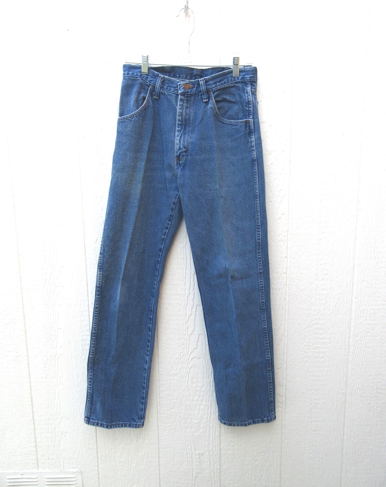 May include: Blue denim jeans hanging on a metal hanger. The jeans have a classic five-pocket design, a button and zipper closure, and a straight leg fit. The denim is a medium wash, showing some fading.