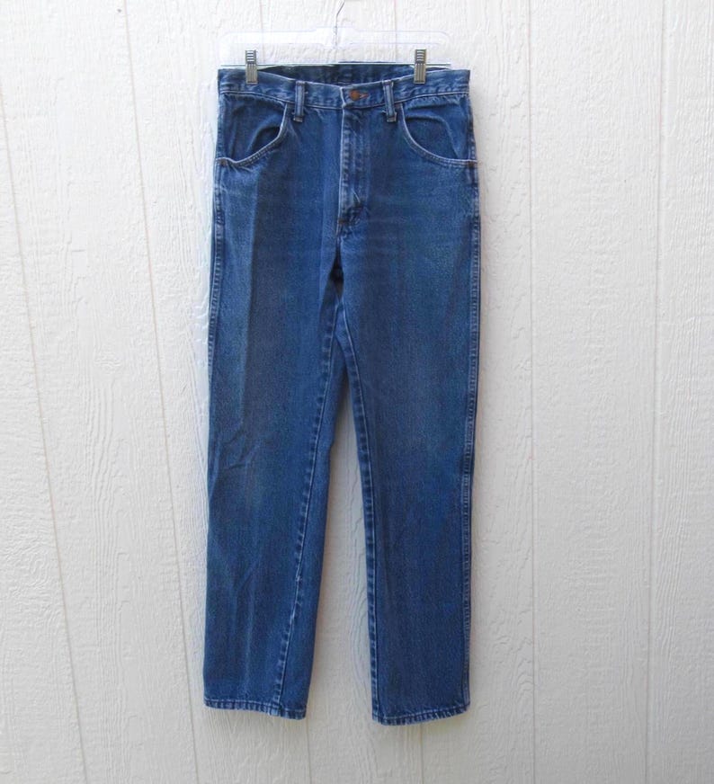 May include: Blue denim jeans hanging on a clear plastic hanger. The jeans have a classic five-pocket design, a button and zipper closure, and a straight leg cut. The denim has a medium wash with some fading.