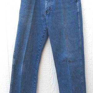 May include: Blue denim jeans with a classic five-pocket design. The jeans are hung on a metal hanger and feature a button and zipper closure. The pants have a straight leg cut and are made of a durable denim material.