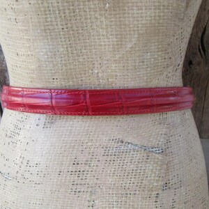 Puede incluir: Un cintur&oacute;n rojo con textura de piel de cocodrilo envuelve un maniqu&iacute;. El cintur&oacute;n es de un tono rojo vibrante y parece estar hecho de cuero. El cintur&oacute;n es un accesorio cl&aacute;sico.