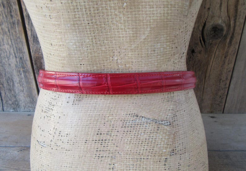 Puede incluir: Un cintur&oacute;n rojo con textura de piel de cocodrilo envuelve un maniqu&iacute;. El cintur&oacute;n es de un tono rojo vibrante y parece estar hecho de cuero. El cintur&oacute;n es un accesorio cl&aacute;sico.