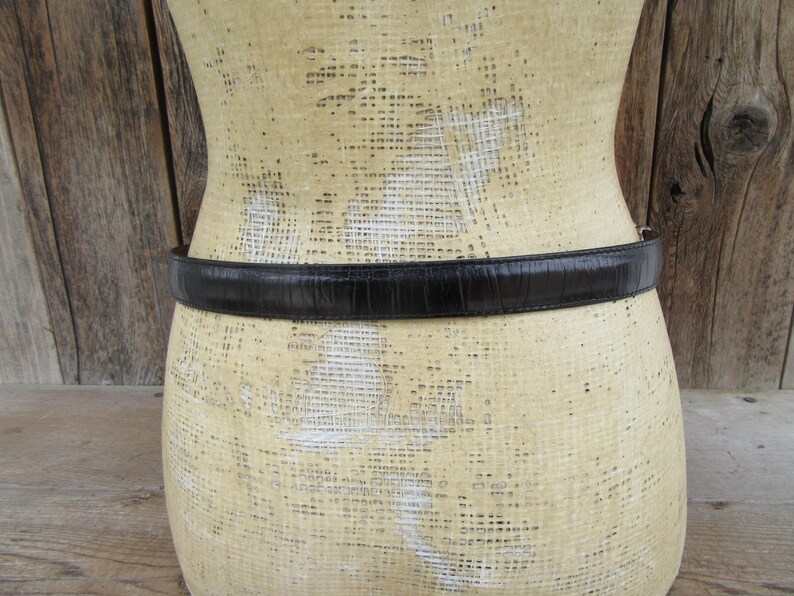 K&ouml;nnte beinhalten: Ein schwarzer G&uuml;rtel mit strukturierter Oberfl&auml;che ist um eine Schaufensterpuppe gewickelt. Der G&uuml;rtel scheint aus Leder oder einem &auml;hnlichen Material zu bestehen. Die Schaufensterpuppe ist beige und hat eine strukturierte Oberfl&auml;che.