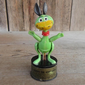 May include: Vintage Hoppy the Hopparoo toy. The green plastic toy features a duck-like face with a yellow beak, black ears, and a red collar. The toy is mounted on a black base with text.