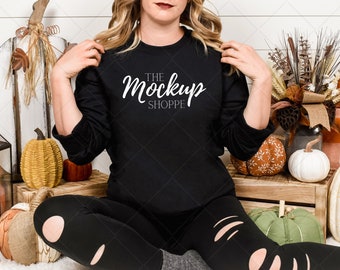 May include: Black long-sleeve shirt with the text "THE Mockup SHOPPE" in white script. The shirt is part of a fall-themed display with pumpkins and decorative elements. The model is wearing black ripped leggings.