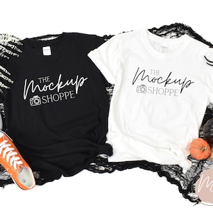 Pode incluir: Duas camisetas em branco, uma preta e outra branca, com o texto "The MockUp Shoppe" impresso em cada uma. As camisetas est&atilde;o dispostas sobre um tecido de renda preto com uma aranha e ab&oacute;boras no fundo.