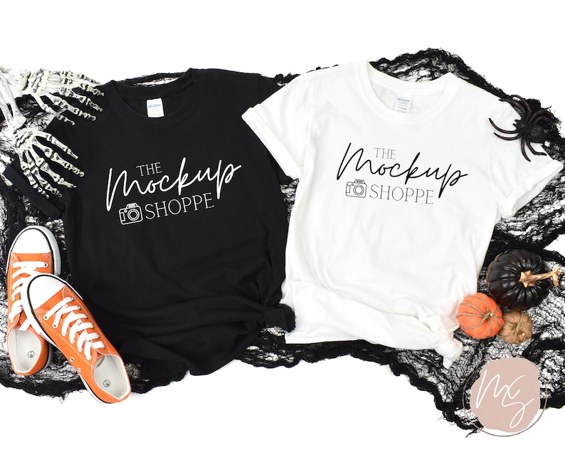 Pode incluir: Duas camisetas em branco, uma preta e outra branca, com o texto "The MockUp Shoppe" impresso em cada uma. As camisetas est&atilde;o dispostas sobre um tecido de renda preto com uma aranha e ab&oacute;boras no fundo.