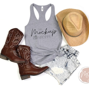 May include: A gray tank top with the text "THE MockUp SHOPPE" and a camera icon. The tank top is styled with denim shorts, cowboy boots, and a straw cowboy hat.