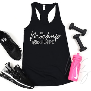 May include: Black racerback tank top with the text "THE MockUp SHOPPE" in white. The tank top is laying flat on a white surface with a pair of black sneakers, two black dumbbells, and a pink water bottle.