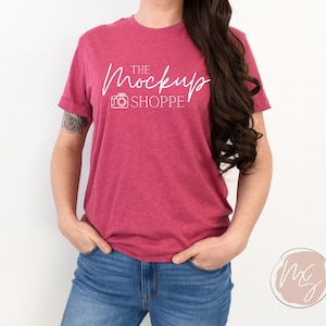 Könnte beinhalten: Eine Frau trägt ein rotes melieres T-Shirt mit dem Text "THE Mockup SHOPPE" und einem Kamerasymbol in Weiß.