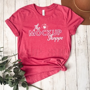 Puede incluir: Una camiseta roja con el texto "The Mockup Shoppe" y un gráfico de cámara con un corazón.