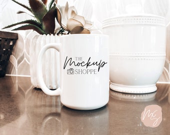 May include: White ceramic coffee mug with a black handle and the text "THE MockUp SHOPPE" with a camera icon. The mug is sitting on a brown countertop.