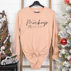 May include: A peach-colored long-sleeved shirt with a knotted front. The shirt has black text that reads "THE Mockup SHOPPE" with a small camera icon.
