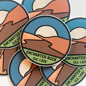 Puede incluir: Una colecci&oacute;n de pegatinas redondas con un dise&ntilde;o de paisaje des&eacute;rtico. Las pegatinas muestran un cielo azul, un sol y monta&ntilde;as marrones y naranjas. El texto "ENCHANTED ROCK ELE. 1,825'" est&aacute; impreso en cada pegatina.