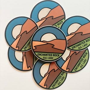 Puede incluir: Un conjunto de pegatinas redondas con un dise&ntilde;o de paisaje que presenta una monta&ntilde;a, un sol y el texto "ENCHANTED ROCK ELE. 1,825'". Las pegatinas tienen una combinaci&oacute;n de colores azul, marr&oacute;n, naranja y crema.