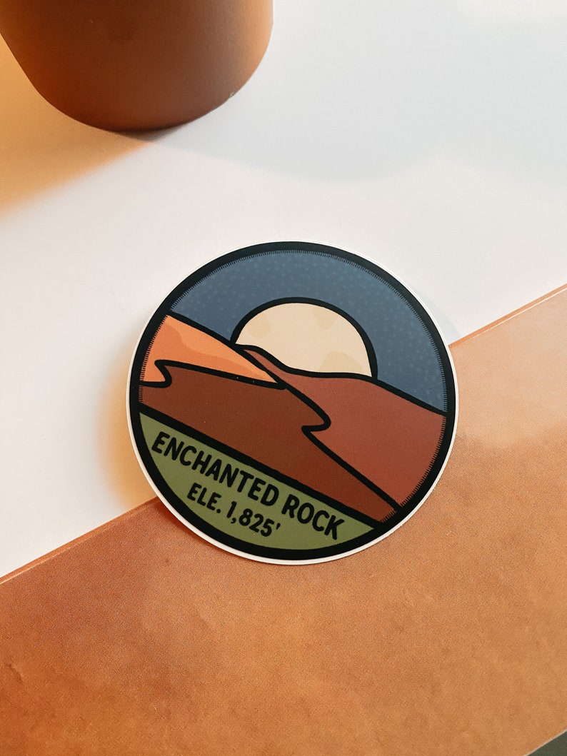 Puede incluir: Pegatina redonda con dise&ntilde;o de paisaje, sol, monta&ntilde;as y texto "ENCHANTED ROCK ELE. 1.825'". Borde blanco y cielo azul oscuro.