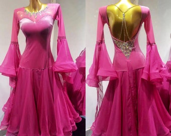 Op de afbeelding: Een roze ballroom dansjurk met een sweetheart halslijn en een lage rug. De jurk heeft een aansluitend lijfje en een zwierige rok met meerdere lagen. Het lijfje is versierd met strass en de rug is versierd met een kralenketting.