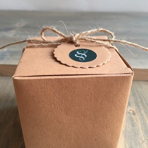 May include: A brown cardboard box with a twine bow and a round tag with a black and silver logo. The logo is a stylized letter "S" with a flourish.