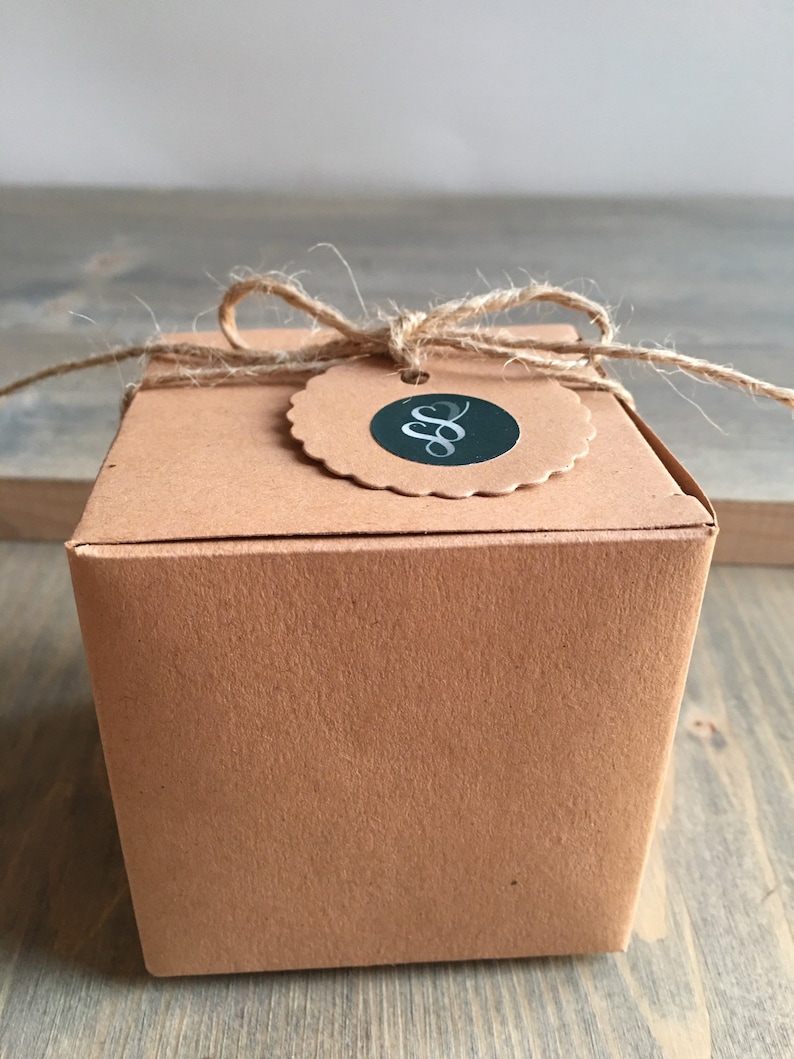 May include: A brown cardboard box with a twine bow and a round tag with a black and silver logo. The logo is a stylized letter "S" with a flourish.