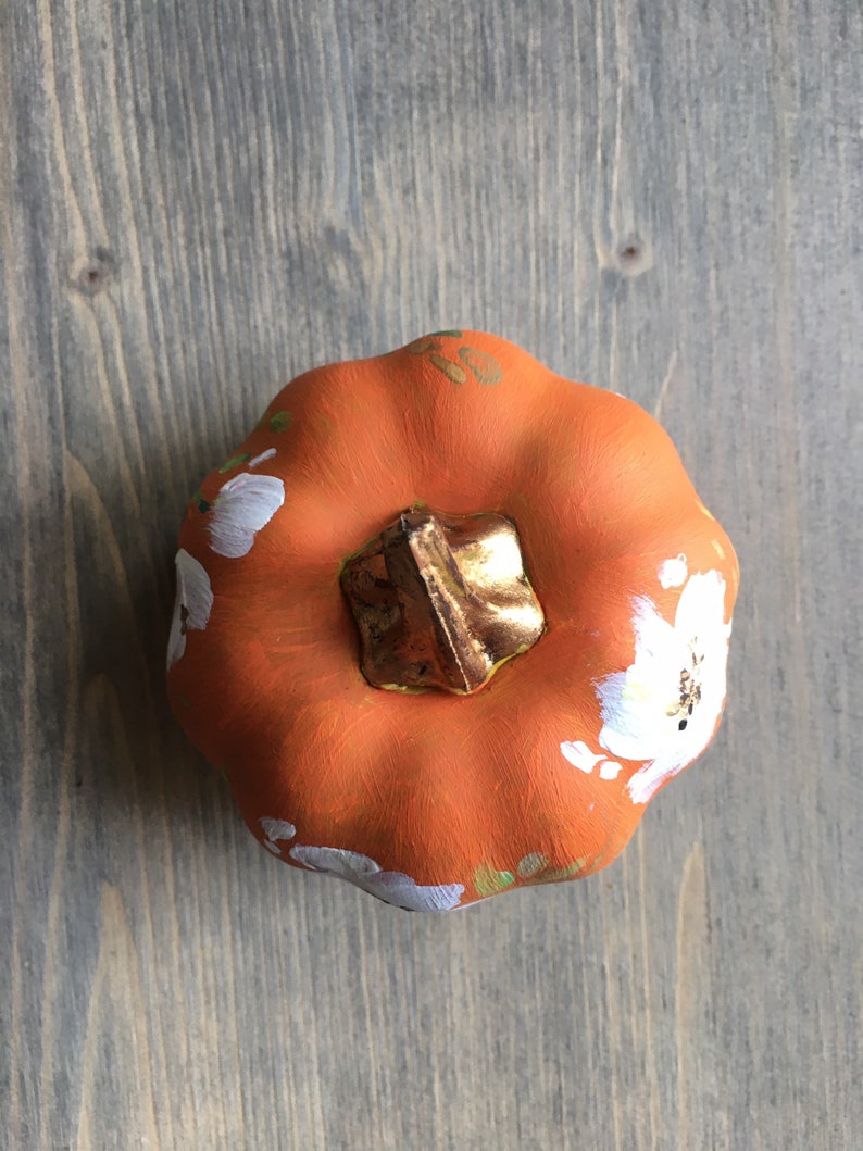 May include: A small orange pumpkin with a gold stem and white painted flowers.