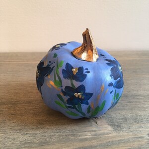 May include: A small blue pumpkin with a gold stem, painted with blue flowers and gold accents.