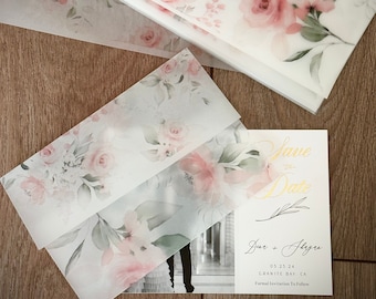 Op de afbeelding: Een stapel doorschijnende perkamentvellen en een bijpassende envelop met een zachte roze bloemenprint en groene bladeren. Daarnaast ligt een rechthoekige Save the Date-kaart met goudkleurige tekst: Save the Date, Dana + Shazad, 05.25.24, Granite Bay, CA.